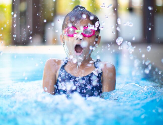A child breaching the surface of a pool with their mouth open taking a breath